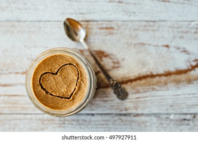 Heart Drawn On Peanut Butter In Glass Jar On Wooden Background