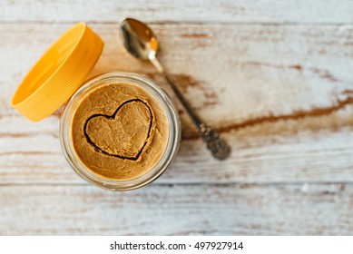 Heart Drawn On Peanut Butter In Glass Jar On Wooden Background