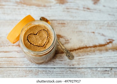 Heart Drawn On Peanut Butter In Glass Jar On Wooden Background