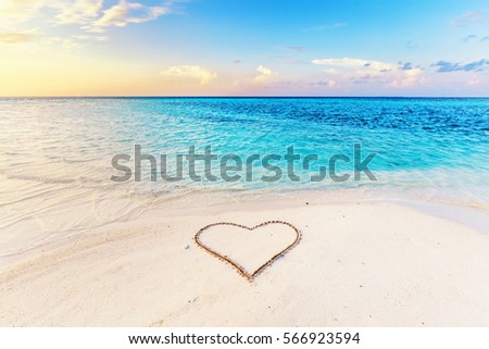 Heart drawn on sand of a tropical beach at sunset. Clear turquoise ocean. Maldives islands.