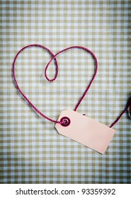 Heart drawn with purple thread through a tag over a checkered fabric pattern - Shutterstock ID 93359392