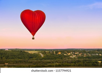 Heart flying red hot air balloon in sunset sky under green village in the forest. - Powered by Shutterstock