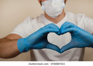 a heart from the hands on the background of a blurry masked man. the concept of love. people's health. blue-gloved hands. - Shutterstock ID 1930087415