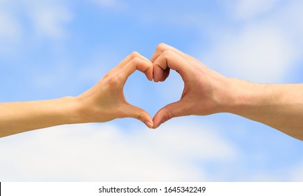 Heart from hands on a sky background. Love, friendship concept. Girl and male hand in heart form love blue sky. Female and man hands in the form of heart against the sky. Closeup.