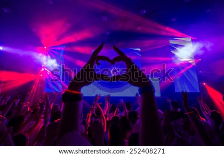 Heart of the hands silhouette on a concert in the center of the heart - DJ visible on the stage.Pink rays laser show.