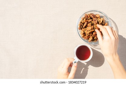 Heart Healthy Snack Tea Break For Coronary Disease - Hand Of A Woman Picking Walnuts From Mix Nuts Bowl And Have A Cup Of Tea In The Other Hand. Improve Blood Pressure, Reduce LDL Cholesterol, Prevent