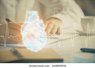 Heart hologram over woman's hands writing background. Concept of Medical education study. Double exposure