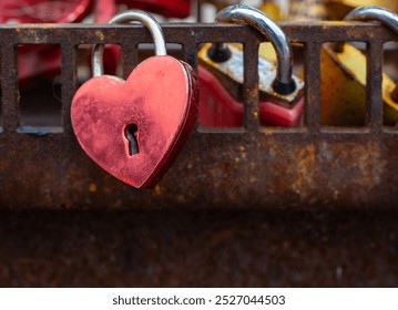 a heart with a keyhole is hanging from a rusty metal fence. The heart is red and has a shiny, metallic appearance. The chain is also metallic - Powered by Shutterstock