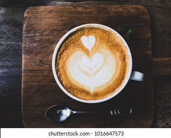 Heart latte art coffee on old wood tray background with stainless steel spoon