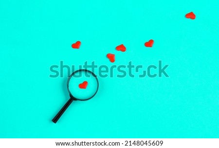 heart lies under a magnifying glass, among many other hearts on a light blue background. The concept of searching for love, find love. Love background. romantic minimalism background. 