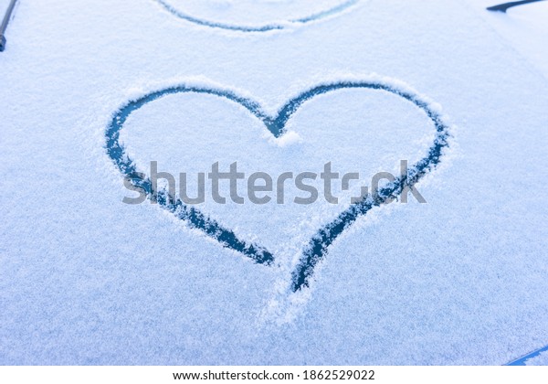 Heart love symbol on windscreen of car in\
snow. View of a snow car after a\
snowfall