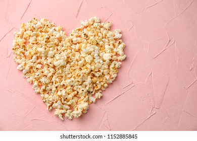 Heart made of delicious popcorn on color background