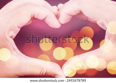 A heart made of two hands is shown in a blurry background. Concept of love and warmth, as the two hands come together to form a heart shape. The blurry background adds a dreamy