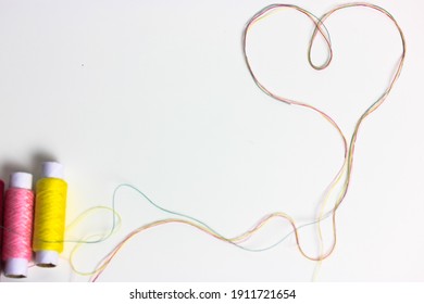 A heart of multicolored thread. Love for sewing and needlework. Threads in the coils on the surface of the white table.