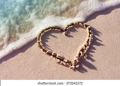 heart on a sand of beach with wave on background