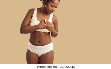 Heart Pain. Woman Pressing On Chest With Painful Expression Having Heart Attack Or Painful Cramps. African American Woman In Underwear Holding Left Side Of Chest On Beige Background. Copy Space.