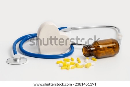 Heart pills near glass bottle, ceramic heart and stethoscope on white background. Cardiology treatment of cardiovascular diseases with medication, dietary supplements and vitamins for heart health.