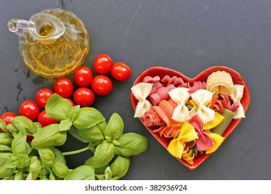 Heart plate with colorful pasta  , tomato, basil , olive oil on black background 