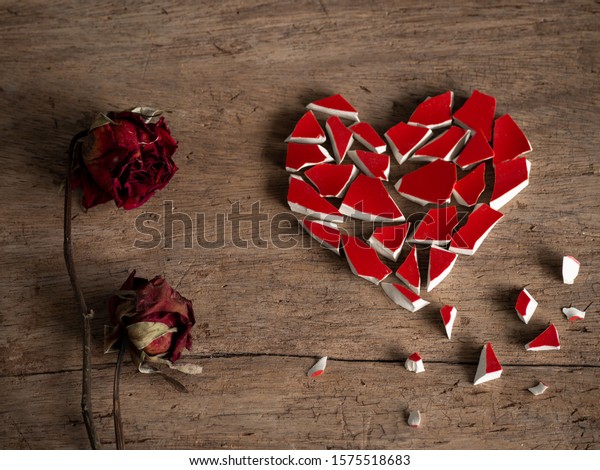 Heart sad couple.Broken heart with broken red\
glass and couple red rose dry on wood background for break my heart\
love,pain,sad. Accompanying sadness article. heart couple or\
poster. valentine concept