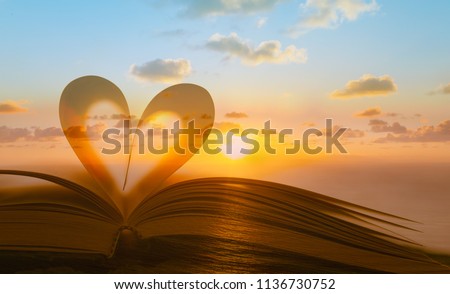 Heart shape from book against peaceful sunset. Reading, religion, love concept. Double exposure. 