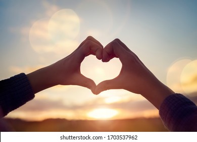 Heart shape with childs hands over sunset sky background - Shutterstock ID 1703537962