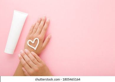 Heart Shape Created From Cream On Young Woman Hand. White Tube. Care About Clean And Soft Body Skin. Closeup. Empty Place For Text On Light Pink Table Background. Pastel Color. 