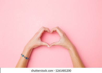 Heart shape created from young woman's hands on pastel pink background. Love and happiness concept. Empty place for emotional, sentimental text, quote or sayings. Closeup. Top view.

