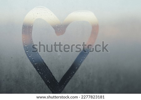 Heart shape drawn on steamy window in front of glowy sunset