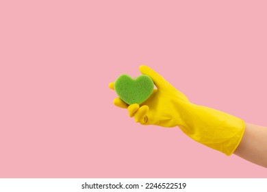 Heart shape green sponge and yellow rubber gloves on pink background. Minimal crative cleaning service concept.