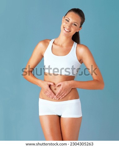 Heart shape, hand gesture on stomach and happy woman in portrait, gut health and wellness isolated on blue background. Weight loss, fitness and healthy female person, self love and bodycare in studio