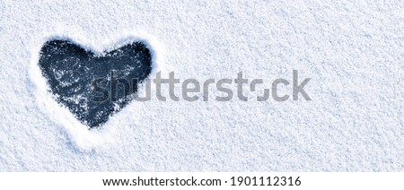 Heart shape love sign, drawn on a snow-covered ice on a winter lake with copy space. Romantic backdrop.
