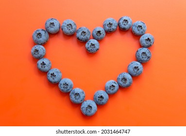 Heart shape made from blueberries on a red background. Heart disease prevention concept.