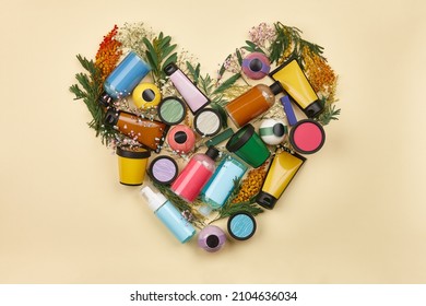 Heart shape made from flowers and cosmetics. Blank body care bottles, beige background.
