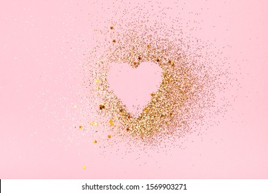 Heart shape made of golden glitter and stars on a pink background. Valentines day, love concept.