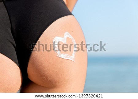 Heart shape made of sun cream on a woman buttocks over the sea background.