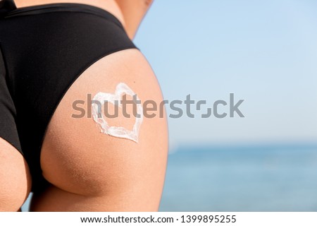 Heart shape made of sun cream on a woman buttocks over the sea background.