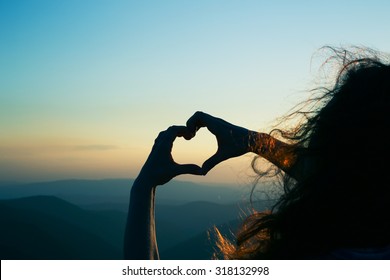 Heart shape. Mountain tourism. Symbol of love. Manifestation of love. Expression of feelings. Enjoy. Girl on a background of mountains. Love and feelings. Long red hair. Wind blowing through her hair.