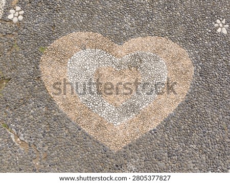 Heart shape pattern made of small pebbles on a stone pavement background. Top view.
