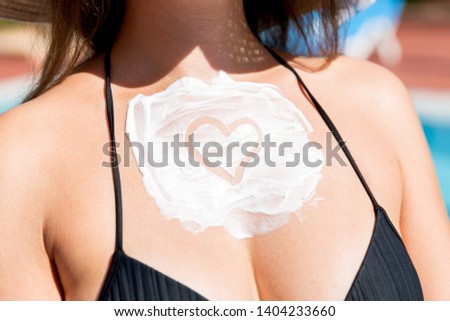 Heart shape sunscreen on woman's breast by the pool. Sun Protection Factor in vacation, concept.