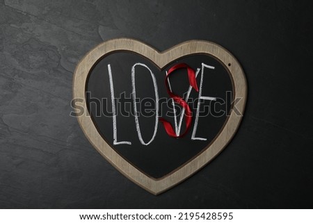 Heart shaped blackboard with word LOVE and letter S of red ribbon on dark background, top view. Composition symbolizing problems in relationship