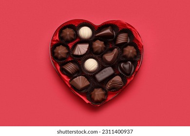 Heart shaped box with delicious chocolate candies on red background, top view