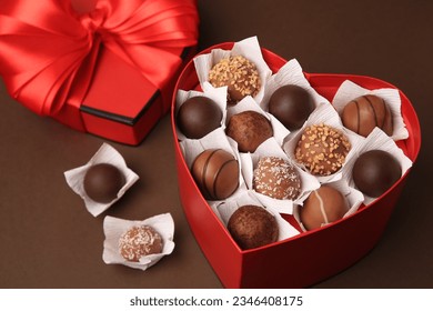 Heart shaped box with delicious chocolate candies on brown background, closeup