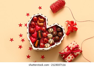 Heart shaped box with tasty chocolate candies and gifts on beige background