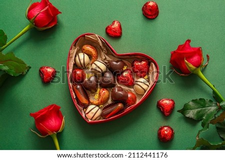 Heart shaped box with tasty chocolate candies and roses on green background