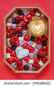 Heart Shaped Candies, Dark And White Chocolate, Strawberries And Cup Of Latte Coffee On Charcuterie Board On Red Background. Close Up, Top View.