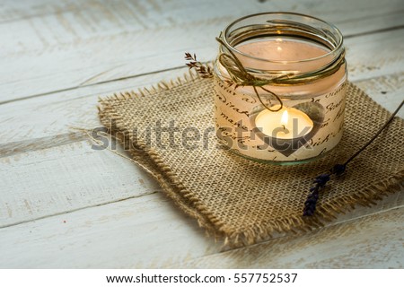 Heart shaped candle in jar with twine and delicate field flower on burlap cloth, white plank wood background, Valentine,wedding decoration,handmade