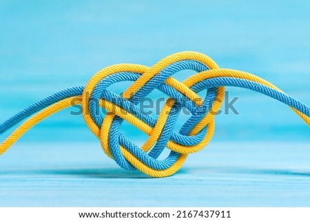 Heart shaped celtic knot made from braided cords painted the colors of the national flag of Ukraine on blue background. Creative unity, faith and protection concept.