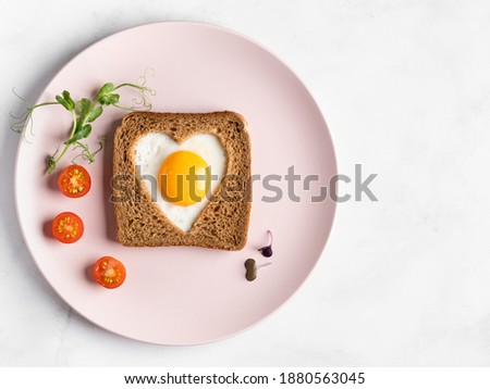 Heart shaped egg in tosted slice of rye bread on pink ceramic plate. St Valentine's day concept. Love breakfast design. Homemade creative food. Healthy sandwich. Festive lunch or breakfast. Copy space