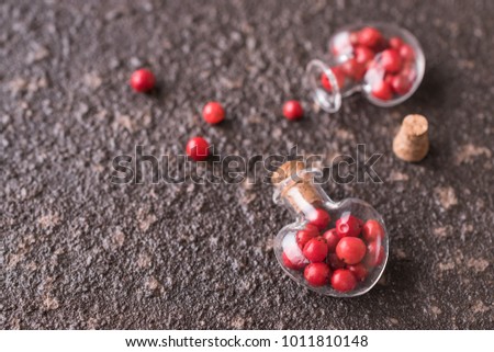 Heart shaped glass bottles filled with rose (brazilian) pepper close up with copypast. Macro photo.