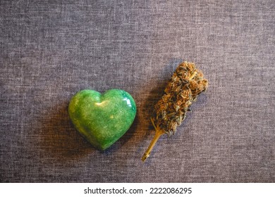 Heart Shaped Green Jade Stone And Big Marijuana Bud (weed Head) Over A Gray Fabric Background